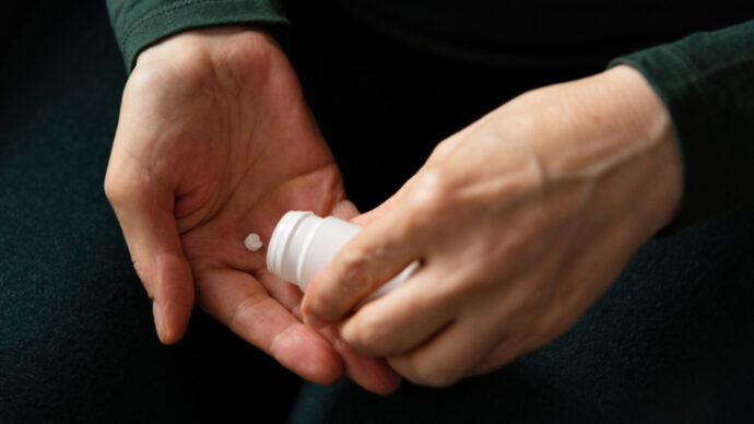 A person holds a white pill bottle, carefully dispensing an abortion pill into their other hand.