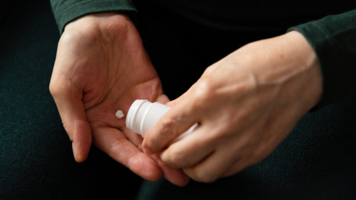 A person holds a white pill bottle, carefully dispensing an abortion pill into their other hand.