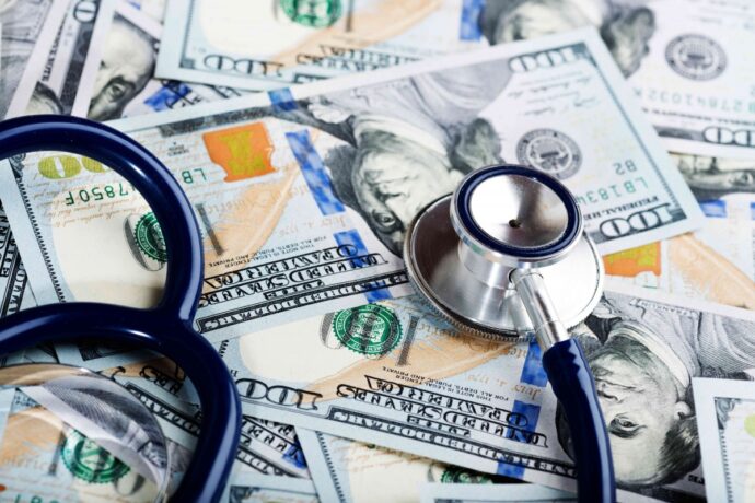A stethoscope rests on a pile of hundred-dollar bills, symbolizing the intersection of healthcare and finance.