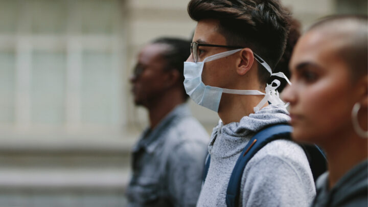 Three people, one wearing a face mask, stroll outdoors. Among them, individuals from diverse backgrounds including Blacks and Latinos, embrace the fresh air while raising awareness about HIV prevention.