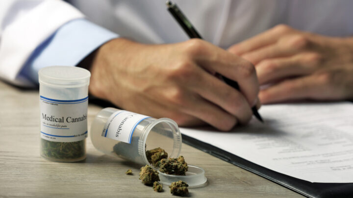 A person writes on a document near two containers labeled "Medical Cannabis," with cannabis buds visible, highlighting its role in cannabis medicine.