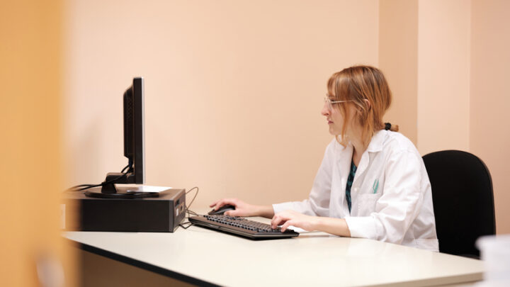 A person in a white lab coat sits at a desk, working on a computer, illustrating the future of healthcare through enhanced physician engagement.