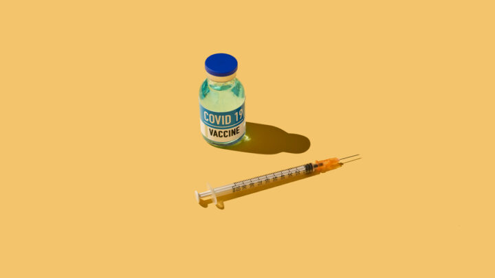 A vial labeled "COVID-19 Vaccine" and a syringe are placed on a yellow background, symbolizing the crucial step of receiving your vaccination.