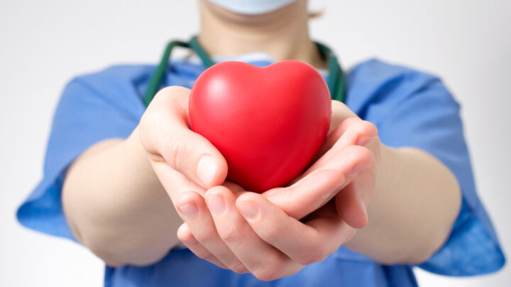 A dedicated physician in blue scrubs gently holds a red heart-shaped object in their outstretched hands, symbolizing hope amidst the ongoing organ shortage crisis.