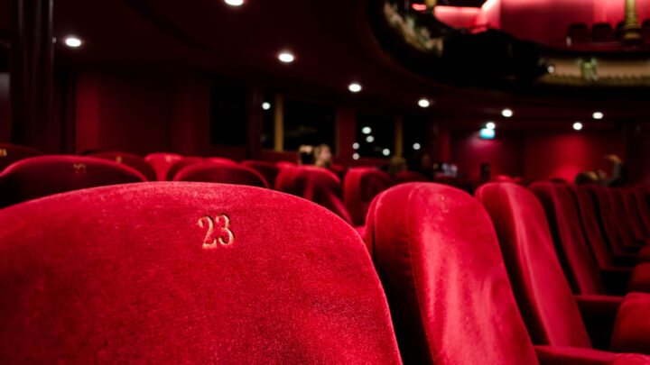 Theater seats in rich red velvet, with seat number 23 prominently in focus, evoke the classic charm of movie theaters under dim lighting.