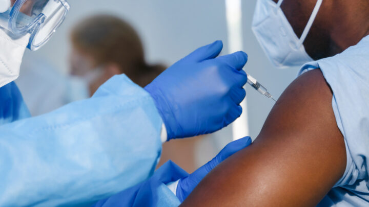A healthcare worker in blue protective gear administers a vaccine to a person's arm, embodying the dedication physicians demonstrate daily.