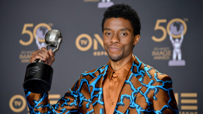 A person in a patterned suit, symbolizing triumph over racial disparities, proudly holds an award trophy. They stand against a backdrop featuring "50" and a figure with a mask, reflecting the perseverance of doctors dedicated to health equity.