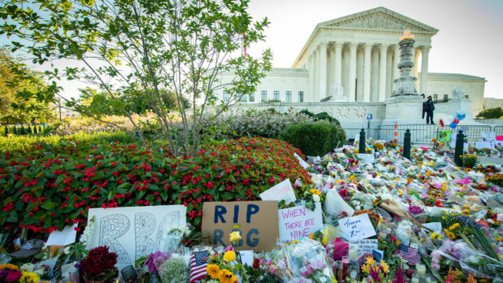 A memorial with flowers and signs stands solemnly in front of a neoclassical building, likely a tribute to RBG's death, honoring the legacy of a significant figure.