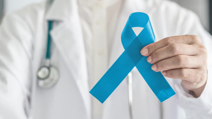 A doctor holds a blue awareness ribbon, challenging traditional expectations of masculinity by promoting the importance of seeking help.