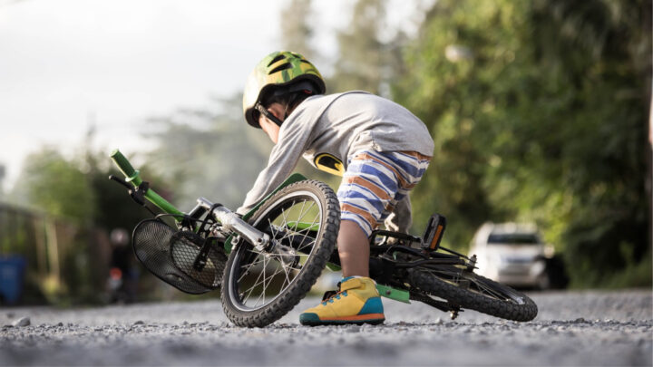 A child wearing a helmet leans over a fallen bicycle on a gravel path, surrounded by greenery on a sunny day, reminiscent of the peaceful scenes from the March 2021 edition.