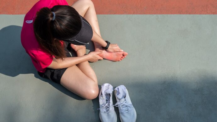 A person from the March 2021 edition is sitting on the ground in athletic attire, holding their foot in discomfort. Sneakers are placed in front of them, reminiscent of a scene solved on Sermo.