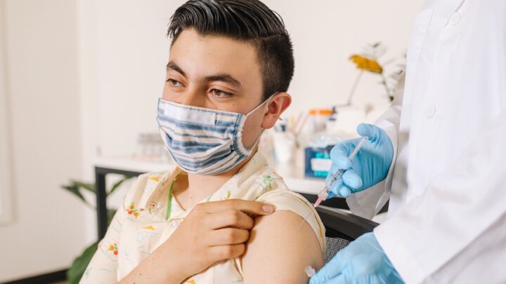 A person wearing a mask receives a vaccine injection from a healthcare worker in a lab coat and gloves, amid concerns over declining vaccine rates.