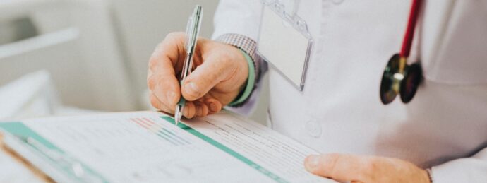 A person in a white coat holds a pen, meticulously updating medical records on a clipboard.