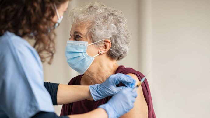 An HCP administers a vaccine to an older adult, who is wearing a mask.