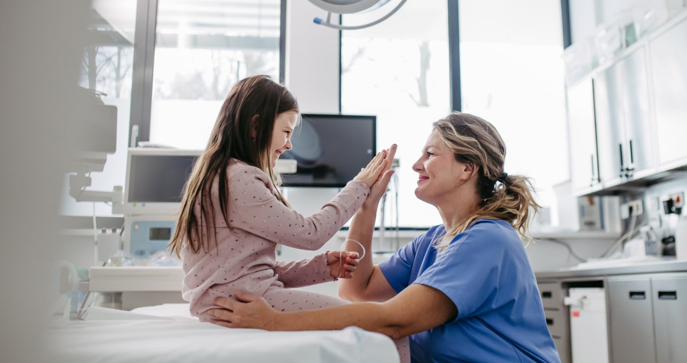 A physician high-fives a young girl sitting on an exam table in a medical room, exemplifying a moment of care and connection that helps improve patient satisfaction.