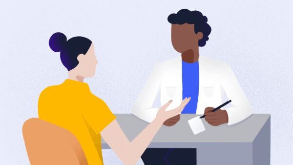 A person in a yellow shirt talks to a doctor in a white coat holding a pen and paper across the table, resembling a patient consultation.