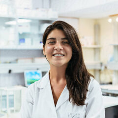 A person in a lab coat, embodying the essence of healthcare credentialing, stands smiling confidently in a laboratory setting.