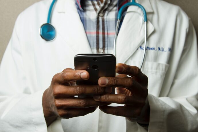 In uncertain times, a doctor in a white coat and stethoscope navigates telemedicine using a smartphone.