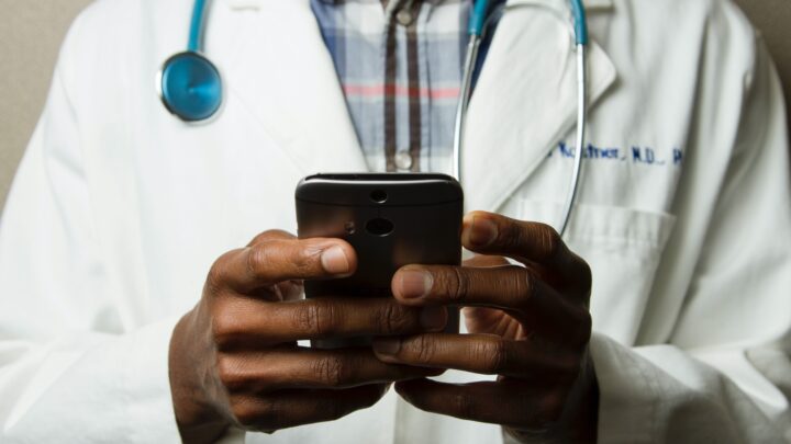 In uncertain times, a doctor in a white coat and stethoscope navigates telemedicine using a smartphone.