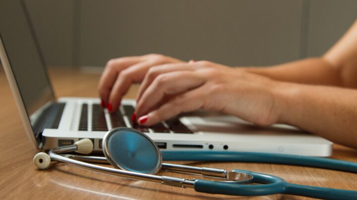 A person types on a laptop next to a stethoscope on a wooden table, reflecting the changing landscape of jobs for Sermo physicians during the pandemic.