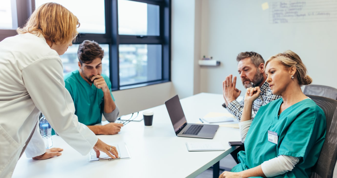 Four healthcare professionals engaged in a lively discussion around a table, surrounded by papers and a laptop, demonstrating leadership in navigating change within healthcare.