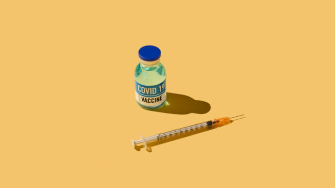 A vial labeled "COVID-19 Vaccine" and a syringe rest on a yellow background, evoking the advancements made by Moderna and Pfizer.