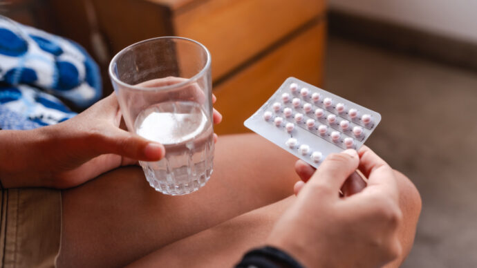 A person holding a glass of water and a blister pack of OTC pills.