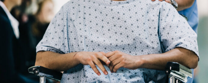 A person in a hospital gown sits in a wheelchair, hands resting on the lap, reminiscent of a case discussed and solved on Sermo, November 2019 edition.