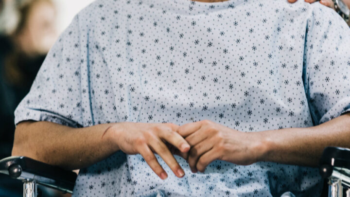 A person in a hospital gown sits in a wheelchair, hands resting on the lap, reminiscent of a case discussed and solved on Sermo, November 2019 edition.