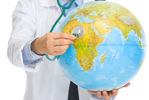 A person in a lab coat uses a stethoscope to listen to a globe, as if offering emergency help to our planet.