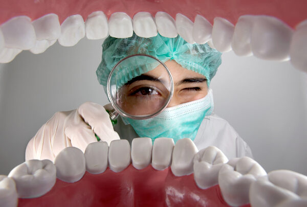 A person in surgical attire, dedicated to oral health, peers through a magnifying glass, offering an intricate view from inside a large model of human teeth.