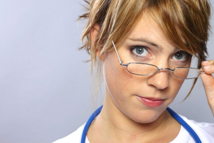 A person with short hair, wearing a stethoscope around their neck and adjusting their glasses, looks confidently at the camera—an embodiment of dedication in the era of AHCA.