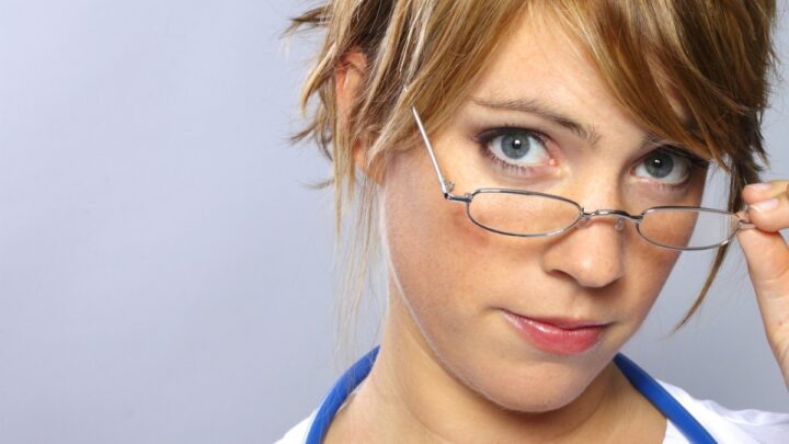 A person with short hair, wearing a stethoscope around their neck and adjusting their glasses, looks confidently at the camera—an embodiment of dedication in the era of AHCA.