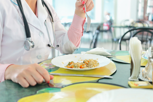 A person in a medical coat is enjoying a plate of rice with vegetables, reminiscent of hospital food, at a table set with placemats and utensils.