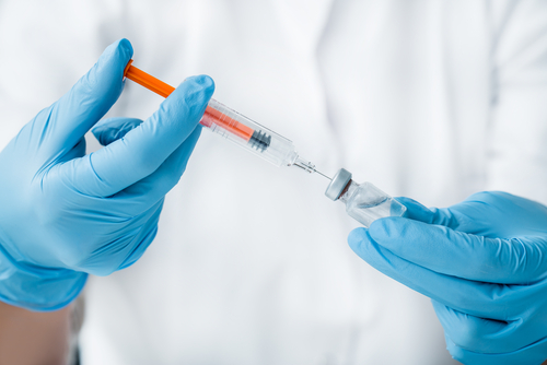 A person in blue gloves carefully draws the flu shot into a syringe from a vial.