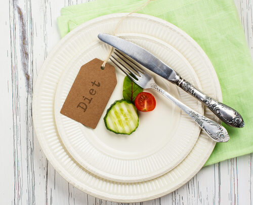 A plate featuring sliced cucumber and tomato, accompanied by a fork and knife, rests on a green napkin atop a white wooden surface. The "Diet" tag subtly emphasizes the healthy theme.