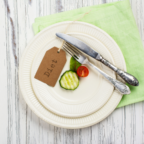 A plate featuring sliced cucumber and tomato, accompanied by a fork and knife, rests on a green napkin atop a white wooden surface. The "Diet" tag subtly emphasizes the healthy theme.