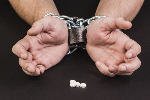Hands chained with metal links, wristband in the center, and three white Suboxone pills on a black background.
