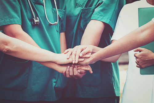 Medical professionals in green and white uniforms place their hands together in a display of teamwork, solidarity, and unwavering support.