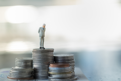 A tiny figurine of a man in a suit stands on a stack of coins, symbolizing financial growth and smart retirement planning.