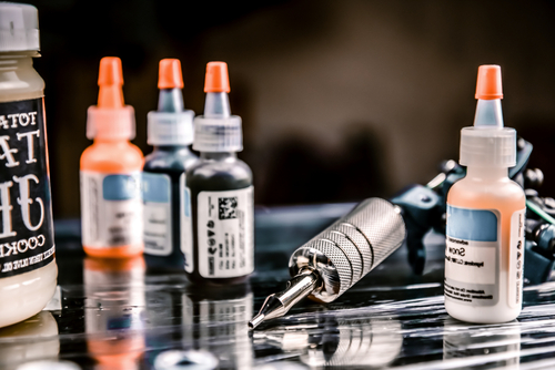 A sleek tattoo machine rests on a metallic surface, encircled by vibrant bottles of ink, ready to create stunning tattoo art.