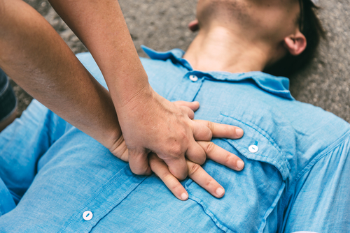 A person urgently performs CPR on an individual in a blue shirt, their focused efforts aiming to revive the motionless figure on the ground.