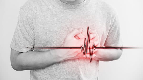 A person in a gray shirt is clutching their chest, with a red heartbeat line overlayed, symbolizing chest pain or heart condition, possibly indicating the need for PFO closure for cryptogenic CVA.
