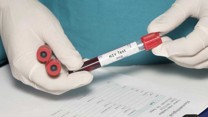 A person wearing gloves carefully holds a test tube labeled "HIV Test" while another test tube and an HIV testing form rest on the table.