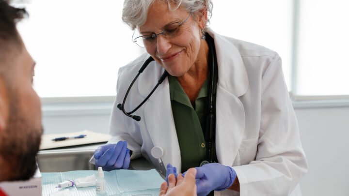 A doctor in a white coat and purple gloves conducts a finger-prick test on a patient, utilizing a small lancet device to ensure accurate results in line with CDC HIV guidelines.