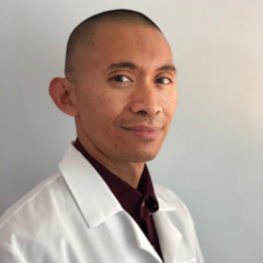 Estylan Dan Arellano, in a crisp white lab coat, stands confidently against a neutral background, looking directly at the camera.