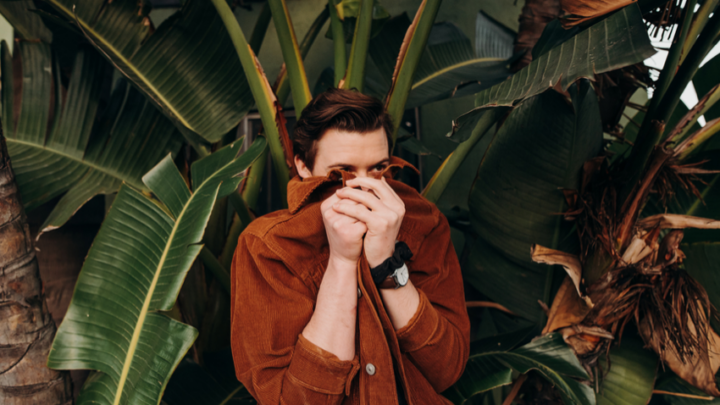 Partially hiding behind their brown jacket, the person is enveloped by the lush green leaves, as if seeking refuge from a looming diagnosis in the air.