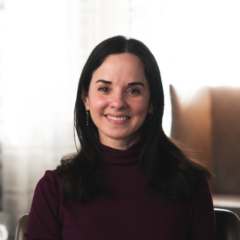 Claudia Martorell, MD, with long dark hair and a maroon turtleneck, smiles warmly while seated indoors.
