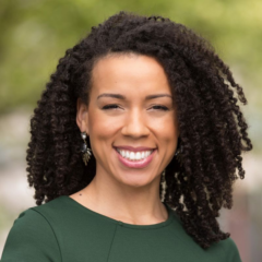 Smiling Rachel Knox, with her curly hair, green top, and earrings, stands outdoors, radiating confidence and charm.
