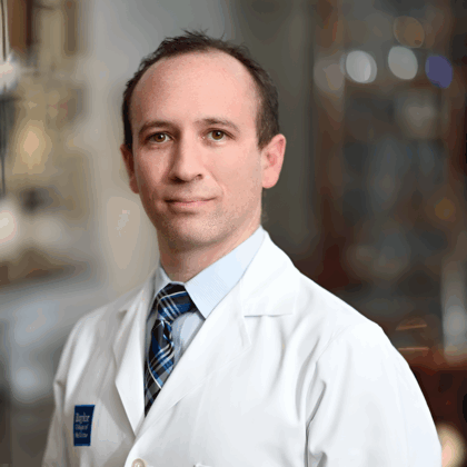 Dr. Bryan Tucker, MD, wearing a white medical coat and striped tie, stands indoors with a blurred background.